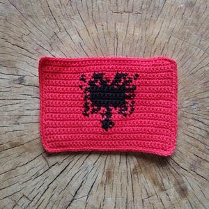 May include: A crocheted red square with a black double-headed eagle in the centre. The eagle is a symbol of Albania.