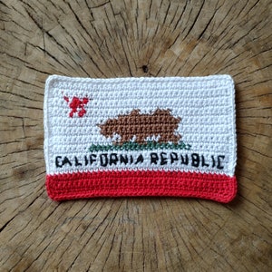 May include: Crocheted California Republic flag with a red, white, and brown color scheme. The flag features a bear and the text "CALIFORNIA REPUBLIC".