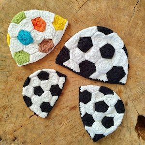 Könnte beinhalten: Vier gehäkelte Mützen in Form eines Fußballs. Eine Mütze ist mehrfarbig mit Grün, Braun, Gelb, Blau und Weiß. Die anderen drei Mützen sind schwarz und weiß.