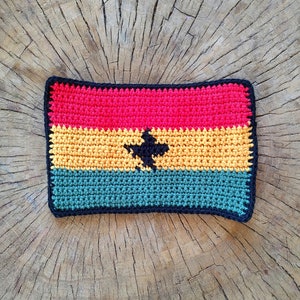 May include: Crocheted flag of Ghana with red, yellow, green, and black colors. The flag is made of yarn and has a black star in the center.