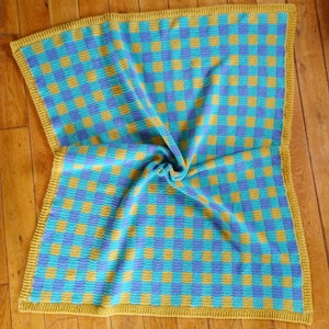 Può includere: Una coperta all'uncinetto con un motivo a scacchi in tonalità di blu e giallo. La coperta ha un bordo all'uncinetto giallo.