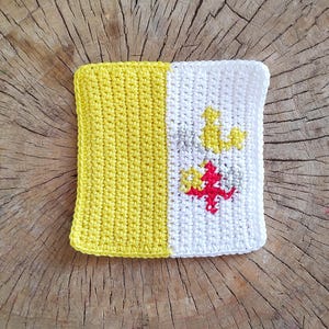 Könnte beinhalten: Ein gehäkeltes Quadrat mit einem gelben und weißen Design. Die weiße Seite zeigt eine rote und graue Blume.
