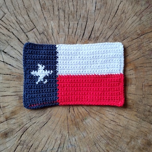 May include: Crocheted Texas flag with a white star on a blue background, a white stripe, and a red stripe.