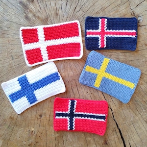 May include: Five crocheted flags, each representing a different country. The flags are red, white, and blue, blue and white, yellow and blue, red and white, and red, white, and black.