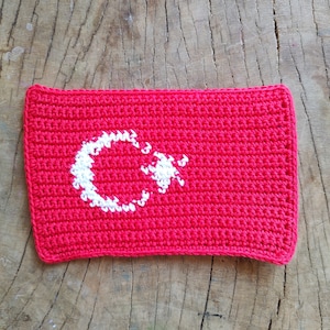 Può includere: Una bandiera rossa all'uncinetto con una mezzaluna e una stella bianche al centro.