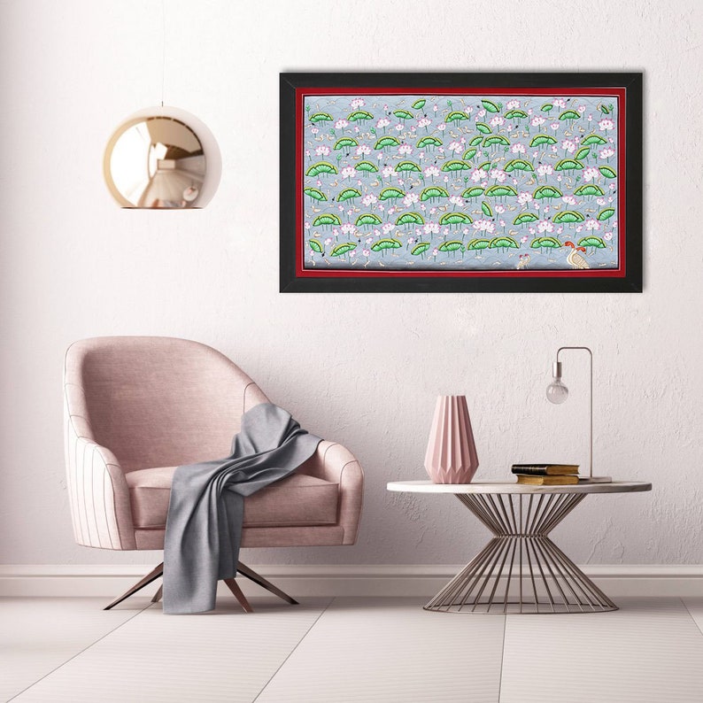 May include: A framed painting depicting a field of pink and green lotus flowers. The painting is set against a light blue background and is framed in black with a red inner border.