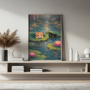 May include: A framed art print depicts two cats in a pond. An orange tabby cat rests on a lily pad, while a black cat peeks out from another. Pink lotus flowers and a bridge are in the background. The artwork is displayed on a shelf.