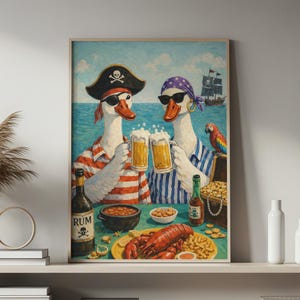 Op de afbeelding: Een ingelijste kunstdruk toont twee ganzen verkleed als piraten die toosten met bierpullen. Ze dragen zonnebrillen, bandana's en een piratenhoed. Een kreeft, friet en een schatkist staan op tafel. Een piratenschip zeilt op de achtergrond.