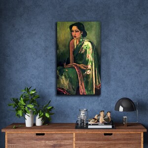 Puede incluir: Una pintura de una mujer que lleva un sari verde y rosa con motivos florales. Est&aacute; sentada con las manos juntas en el regazo y mirando hacia un lado. El fondo es de color verde oscuro.