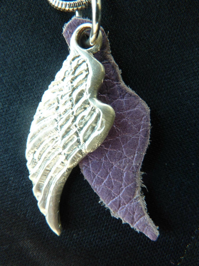 May include: A silver wing pendant with a textured surface, attached to a purple leather cord.