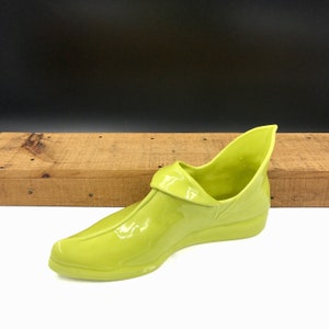 May include: A bright green ceramic shoe-shaped planter. The planter has a pointed toe and a curved heel. The planter is made of a smooth, glossy ceramic.