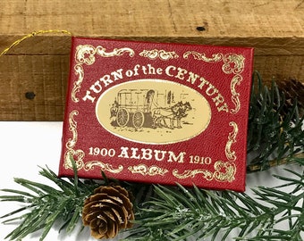 Pode incluir: Uma caixa vermelha com detalhes dourados e o texto "Turn of the Century 1900 Album 1910" na frente. A caixa apresenta uma ilustração vintage de uma carroça puxada por cavalos.