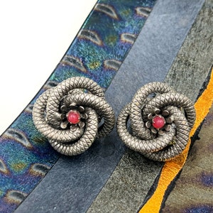 May include: A pair of silver earrings shaped like a flower with a pink center stone.