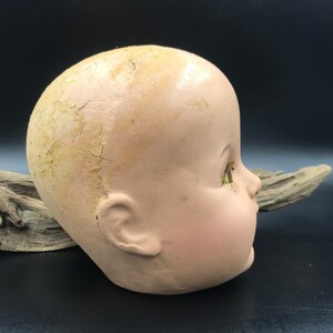 May include: A vintage doll head with cracked and peeling paint. The doll has green glass eyes and a painted smile. The head is made of a hard, plaster-like material.