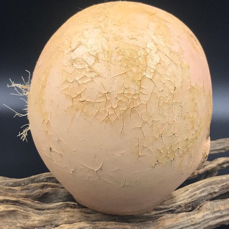 May include: A round, pale pink ceramic object with a cracked, aged finish. The surface is covered in a network of fine cracks, giving it a distressed look. The object is smooth and slightly textured.