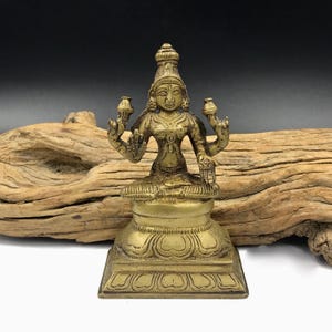 May include: A gold-colored brass statue of a Hindu deity, sitting in a meditative pose with four arms. The statue is on a square base with intricate carvings.