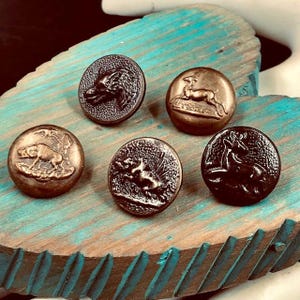 May include: Five circular metal buttons featuring raised relief designs of various animals including a wolf, a deer, a boar, and a horse. Each button has a distinct metallic finish, ranging from dark bronze to lighter copper tones, with textured backgrounds.