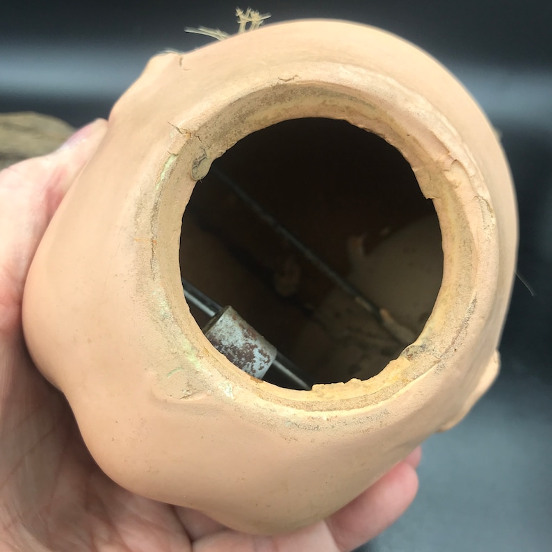 May include: Close-up of the back of a porcelain doll head, showing the opening for the doll's mechanism. The opening is circular and has a rough, unfinished edge. A metal rod is visible inside the opening.