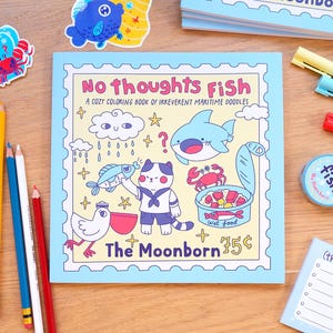 May include: A square coloring book titled No Thoughts Fish, A Cozy Coloring Book of Irreverent Maritime Doodles by The Moonborn 75 cents. The cover features a cartoon cat, a shark, a crab, a bird, and a can of wet food in a light blue frame.