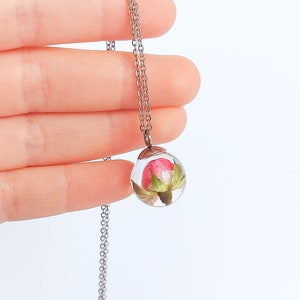 From my outstretched fingers on a white background hangs this beautiful creation under the soft light of my window. The pendant looks crystal clear and bright, covering the soft rose, well-arranged and full of energy to beautify you.