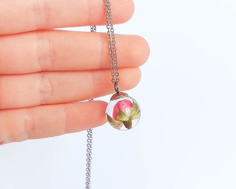 From my outstretched fingers on a white background hangs this beautiful creation under the soft light of my window. The pendant looks crystal clear and bright, covering the soft rose, well-arranged and full of energy to beautify you.