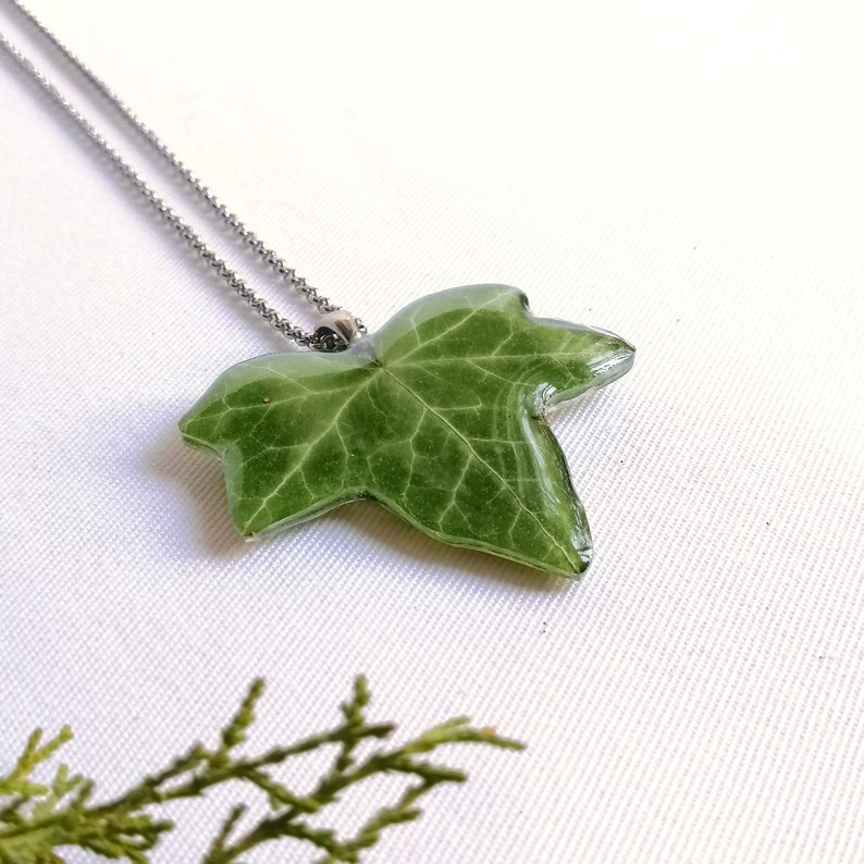 A lovely red leaf necklace appears on a luminous white background. A wonderful piece of nature in this unique handmade creation. Natural light gives it an endearing and iridescent glow. Luminous, transparent and crystalline ivy pendant made for you