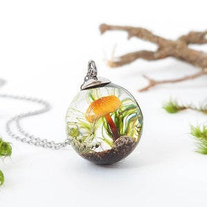 Magical little forest terrarium pendant. Inside, a beautiful mushroom surrounded by natural elements (real moss, a small dandelion seed, a little flower, a shell, and sand). The resin provides an optical effect that magnifies its interior.