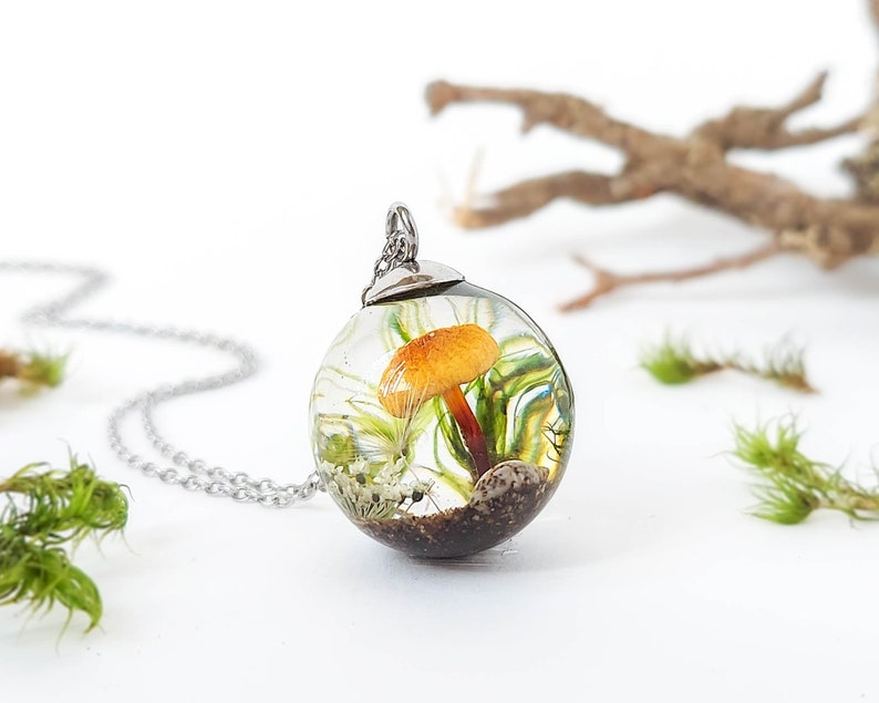 Magical little forest terrarium pendant. Inside, a beautiful mushroom surrounded by natural elements (real moss, a small dandelion seed, a little flower, a shell, and sand). The resin provides an optical effect that magnifies its interior.