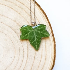 A radiant real ivy leaf pendant appears on a wooden log. Radiant transparent pendant with a real leaf collected from the mountains where I live. Hypoallergenic stainless steel chain. The most perfect nature creation for you or whoever you want.