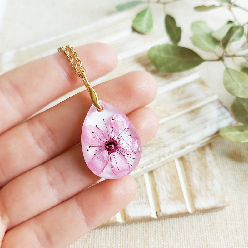 This jewel appears here dangling between my fingers. You can see every detail of the cherry blossom inside. Pink predominates on a white background.