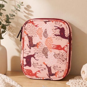 May include: A rectangular zippered storage case in a soft pink hue, featuring a repeating pattern of stylized deer in shades of dark red, orange, and brown, interspersed with white floral-like bursts and thin branch motifs.
