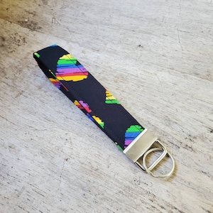 Puede incluir: Llavero negro con un patrón de corazón arcoíris y un anillo de llave plateado.