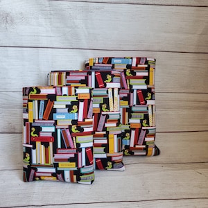 Puede incluir: Tres cubiertas de libros con fondo negro y un patr&oacute;n colorido de libros apilados con t&iacute;tulos como "Qu&iacute;mica", "Ingl&eacute;s" y "Diccionario". Cada cubierta de libro tiene un peque&ntilde;o gusano verde con gafas.