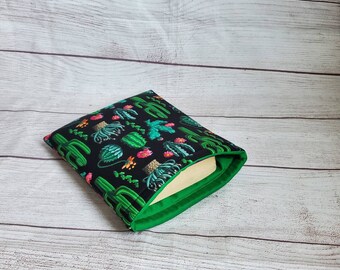 May include: A green and black book cover with a cactus pattern. The cover is folded over a book.