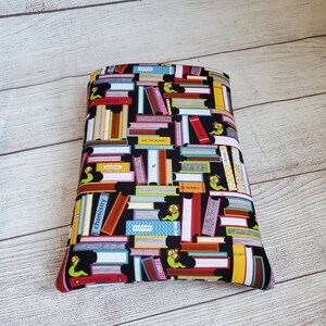 Puede incluir: Bolsa de cremallera de tela negra con tem&aacute;tica de libros con un estampado colorido de libros apilados y gusanos de libros. Los libros tienen t&iacute;tulos como "Ingl&eacute;s", "Historia", "Qu&iacute;mica" y "Diccionario".