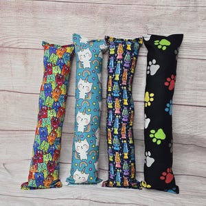 May include: Four colorful catnip toys, each with a different pattern. The toys are made of fabric and are about 10 inches long. The patterns include cats, unicorns, lava lamps, and paw prints.