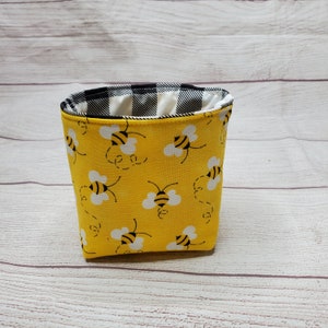 May include: A yellow fabric storage bin with a black and white checkered lining. The bin is decorated with a repeating pattern of black and yellow bees.