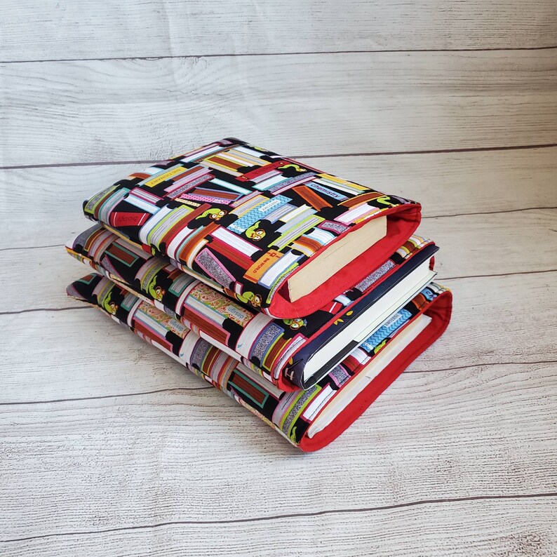 Puede incluir: Una pila de tres cubiertas de libros con un ribete rojo. La cubierta superior presenta un fondo negro con un patr&oacute;n colorido de libros apilados. Las dos cubiertas inferiores son negras con un patr&oacute;n blanco y colorido de libros apilados.