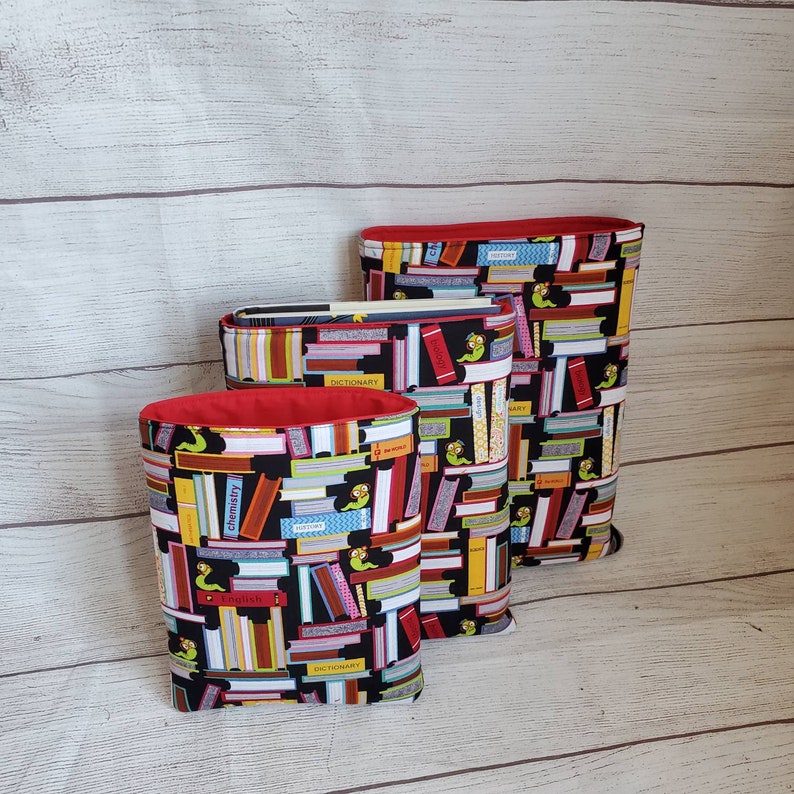Puede incluir: Tres fundas para libros de diferentes tama&ntilde;os con fondo negro y un patr&oacute;n colorido de libros apilados y t&iacute;tulos de libros. Las fundas tienen un forro rojo.