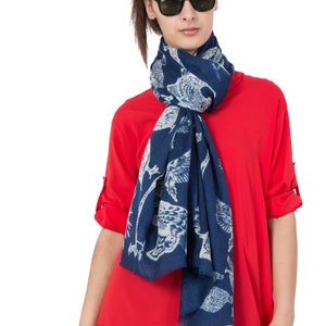 May include: A woman wearing a red shirt and black pants with a blue scarf with a white bird pattern. She is wearing sunglasses.