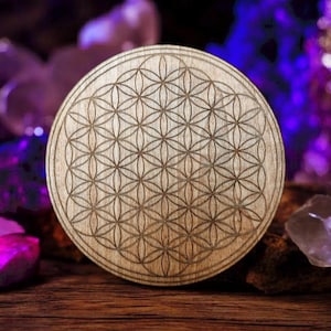 Könnte beinhalten: Eine runde Holzscheibe mit einem lasergravierten Lebensblume-Muster. Die Scheibe ist von violetten Kristallen und einer brennenden Kerze umgeben.