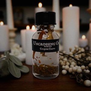 May include: A clear glass bottle with a black cap, filled with liquid and herbs. The bottle has a black label that reads "Uncrossing Oil with Rue Conjure Crafts". The background features lit candles and white berries, creating a mystical ambiance.