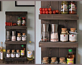 May include: A dark brown wooden spice rack with three shelves. The top shelf has two glass jars of pesto sauce, a small bowl of red tomatoes, and a jar of red sauce. The middle shelf has two silver pepper grinders, a jar of salt, a jar of dried herbs, and a jar of spices. The bottom shelf has three jars of spices, a bottle of oil, and a bottle of vinegar.