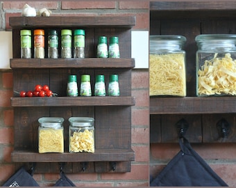 May include: A rustic wooden shelf unit with three shelves and two hooks. The shelves are filled with glass jars of pasta and spice bottles. The unit is mounted on a brick wall.