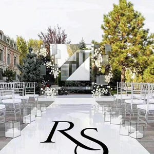 Puede incluir: Montaje para una ceremonia de boda al aire libre con un pasillo blanco y sillas transparentes. Un telón de fondo geométrico espejado está decorado con flores blancas. El pasillo presenta las iniciales "RS" en negro.