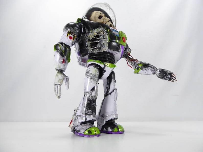 May include: A modified Buzz Lightyear action figure with a skeletal head inside the helmet. The toy has a black, white, green, and purple color scheme, with exposed wiring and battle damage details. The figure is posed against a white background.