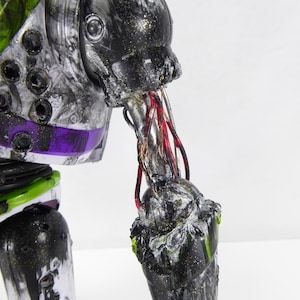 May include: A close-up of a distressed Buzz Lightyear action figure. The toy's arm is torn, revealing wires. The figure has a black, silver, green, and purple color scheme. The toy's arm is damaged, with exposed wires.
