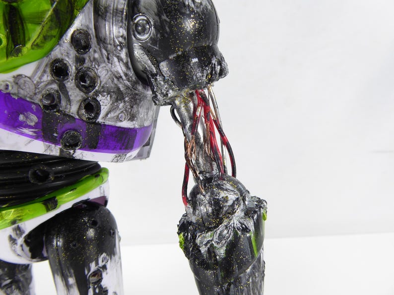 May include: A close-up of a distressed Buzz Lightyear action figure. The toy's arm is torn, revealing wires. The figure has a black, silver, green, and purple color scheme. The toy's arm is damaged, with exposed wires.