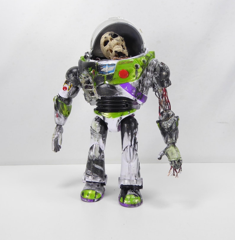 May include: A modified Buzz Lightyear action figure with a skeletal head inside the helmet. The toy is painted in a zombie-like style, with exposed wires and decaying details. The figure's colors include green, white, black, and purple.