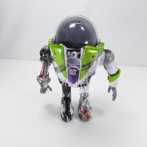 May include: A Buzz Lightyear action figure with a clear plastic body, green and purple accents, and a dark gray helmet. The figure has articulated limbs and a detailed design, showcasing a futuristic space ranger aesthetic.